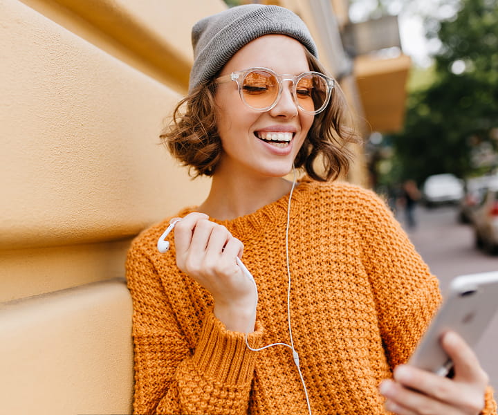 Smiling woman in orange sweater looking at her phone.